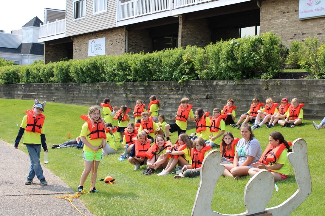 Students in life jackets sitting in the grass. 