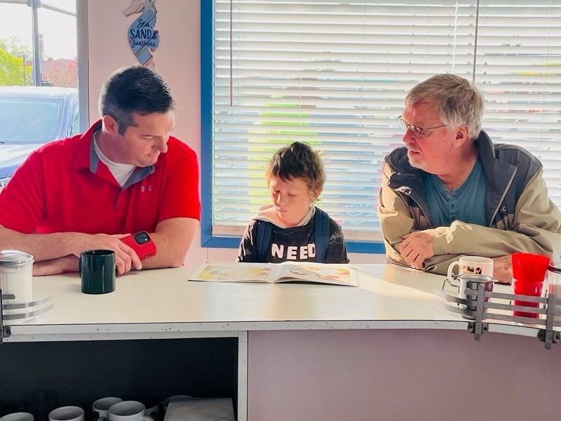 Two men and a boy sitting at a counter reading a book